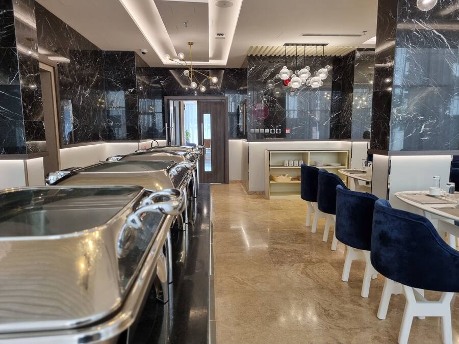 A modern restaurant with marble walls, a long counter with metal trays, and blue chairs.