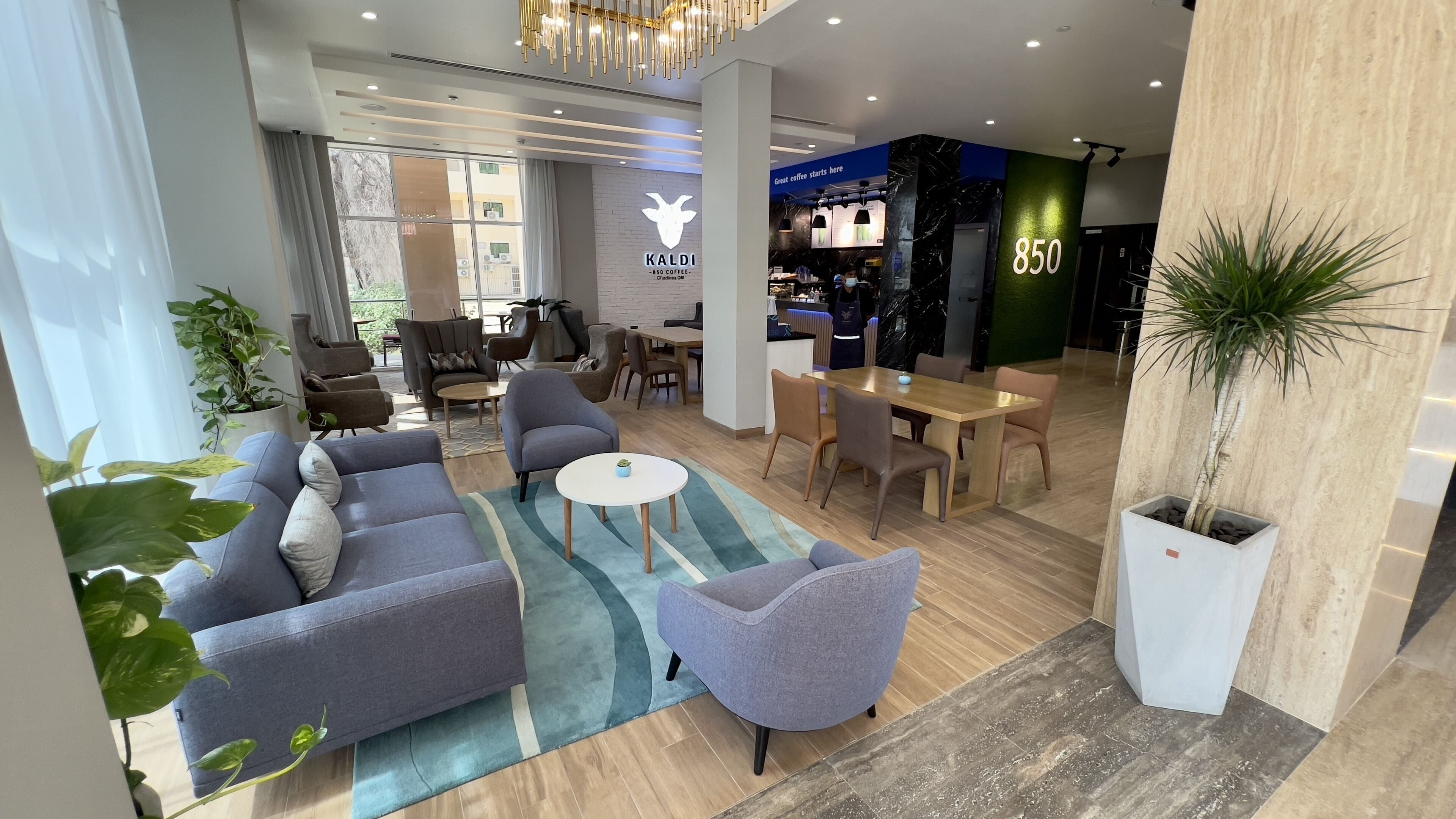 A modern hotel lobby with seating areas, a coffee bar, and a reception desk.