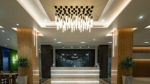 A modern reception area with a geometric wall design, a central staircase, and two potted plants. - Citadines Al Ghubrah Muscat (Muscat)