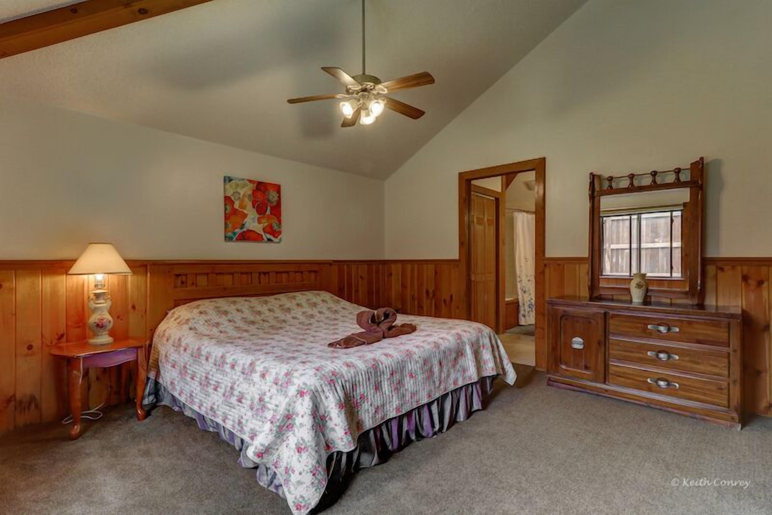 A bedroom with a bed, wooden headboard, a ceiling fan, a dresser, and a mirror.