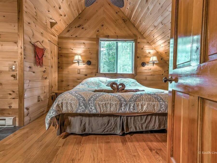 Une chambre confortable, aménagée dans un chalet en bois, avec un lit, deux lampes fixées au mur et une fenêtre.