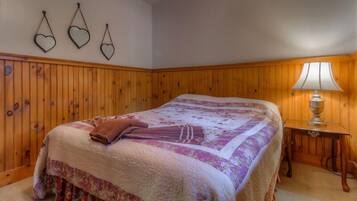 A bedroom with a large bed, wooden paneling on the walls, a bedside table with a lamp, and three heart-shaped wall decorations.