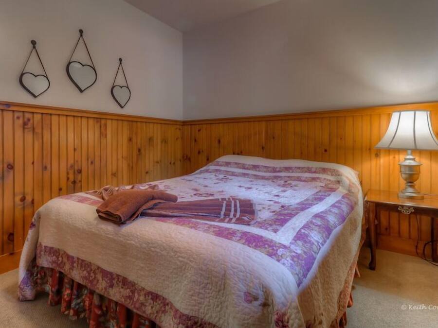 A bedroom with a large bed, wooden paneling on the walls, a bedside table with a lamp, and three heart-shaped wall decorations.