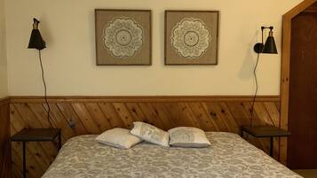 Une chambre à coucher avec une tête de lit en bois, un lit recouvert d’une literie à motifs, deux lampes fixées au mur et deux éléments décoratifs muraux.