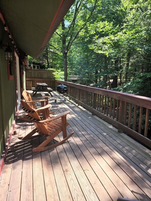 A wooden deck with rocking chairs and a grill, overlooking a forested area.