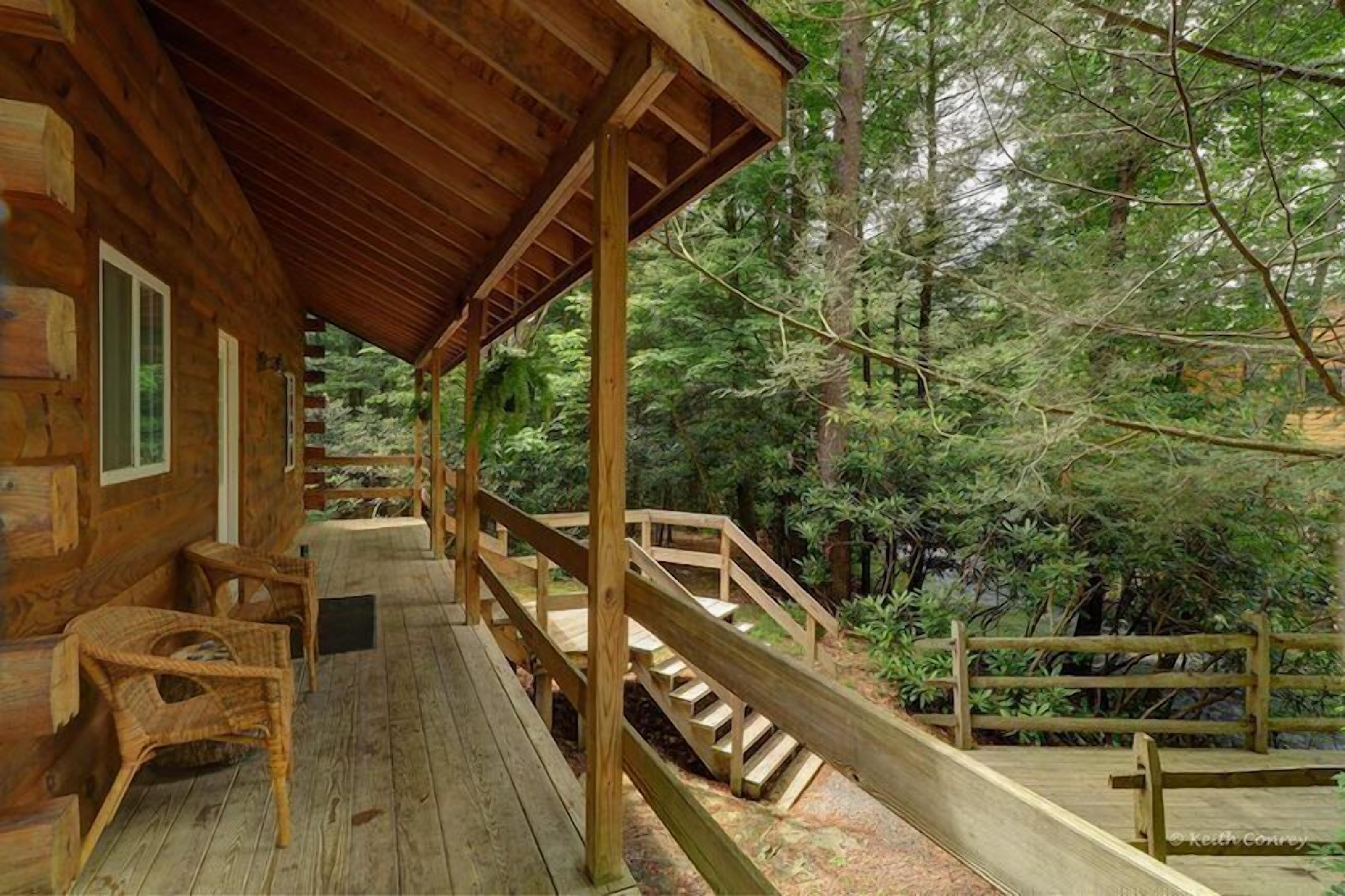 A wooden cabin with a covered porch, wooden stairs, and wicker chairs.