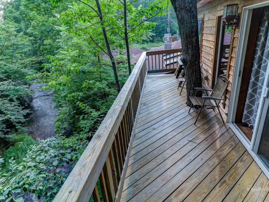 A wooden deck with a view of a forested area and a stream.