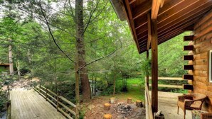A wooden deck with a fire pit, surrounded by trees, and a covered seating area with chairs. - Magnolia Streamside Resort (Canadensis)