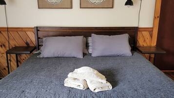 Una cama con una manta gris texturizada, dos almohadas y una toalla blanca doblada. Encima de la cama, hay dos paneles decorativos montados en la pared.