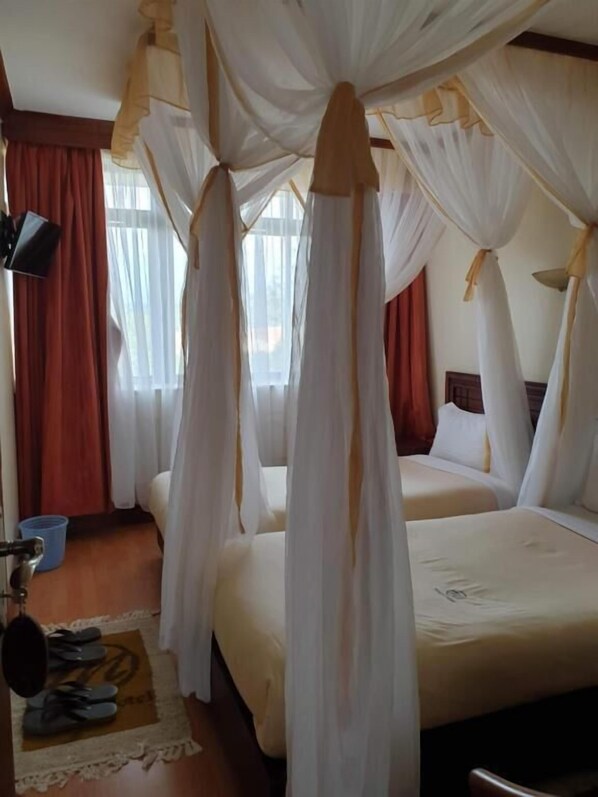 A room with a bed under a canopy, a desk with a chair, and a window with curtains.