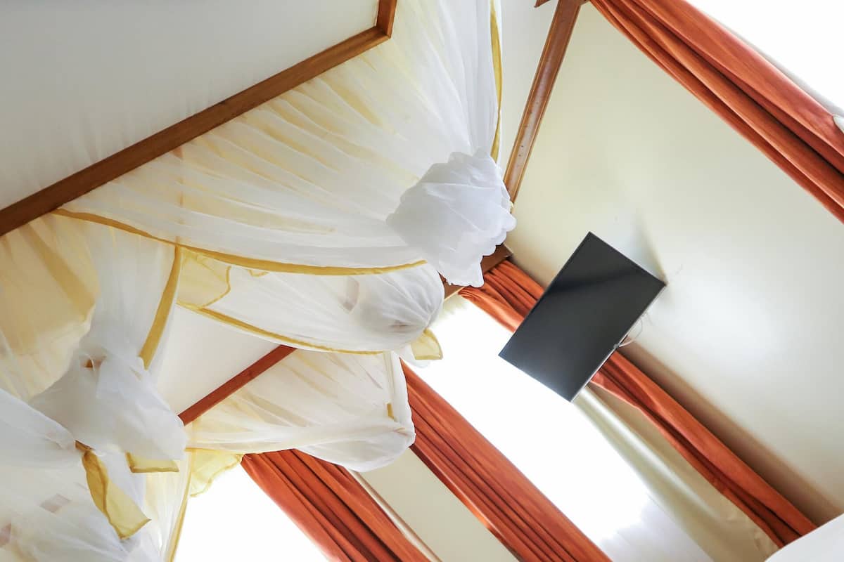 Una habitación con una cama cubierta con cortinas blancas y amarillas, un objeto negro en la pared y cortinas rojas.