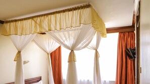 A room with a canopy bed, a wooden headboard, and a window with orange curtains. - Maxoil Hotel (Nanyuki)