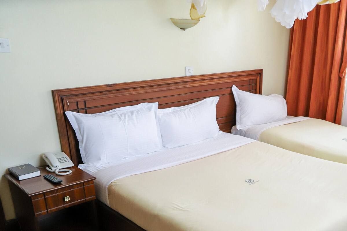 Habitación de hotel con cama doble, mesita de noche con teléfono y libro, y ventana con cortinas.