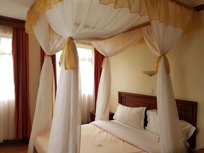 A bedroom with a canopy bed, a wooden headboard, and a bedside table. - Maxoil Hotel (Nanyuki)