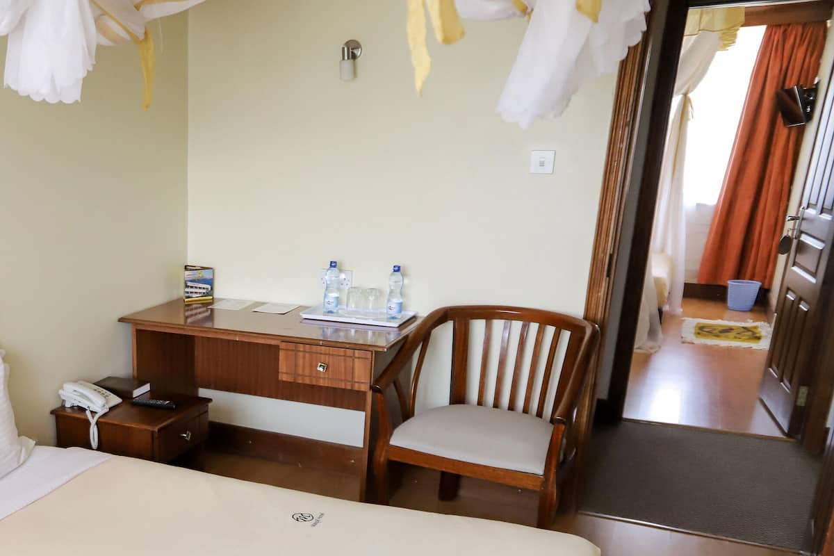 Una habitación de hotel con cama, escritorio de madera, silla, mesita de noche y espejo.