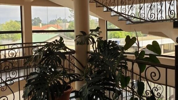 A spacious indoor area with a polished floor, a staircase with ornate railings, and large potted plants. - Maxoil Hotel (Nanyuki)