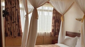 A bedroom with a bed under a canopy, a wooden headboard, and a patterned bedspread. - Maxoil Hotel (Nanyuki)