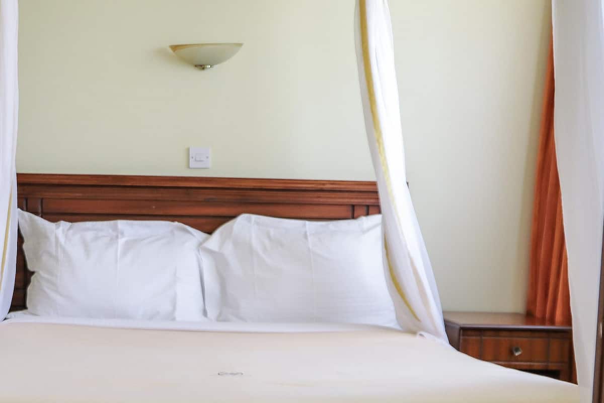 Una cama con ropa de cama blanca, cabecera de madera y lámpara fijada a la pared.