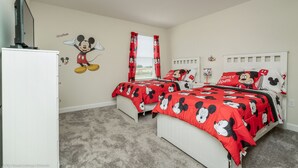 Et soveværelse med to senge, begge med sengetøj med Mickey Mouse-tema, et fjernsyn på et skab og et vindue med røde gardiner.