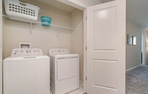 A laundry room with two front-loading washing machines and a dryer, a white door, and a shelf with laundry baskets.