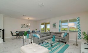 A modern living room with a sectional sofa, a glass coffee table, and a dining area with a glass-top table.