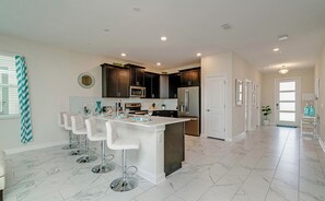 A modern kitchen with a central island, bar stools, dark cabinetry, and a white door.