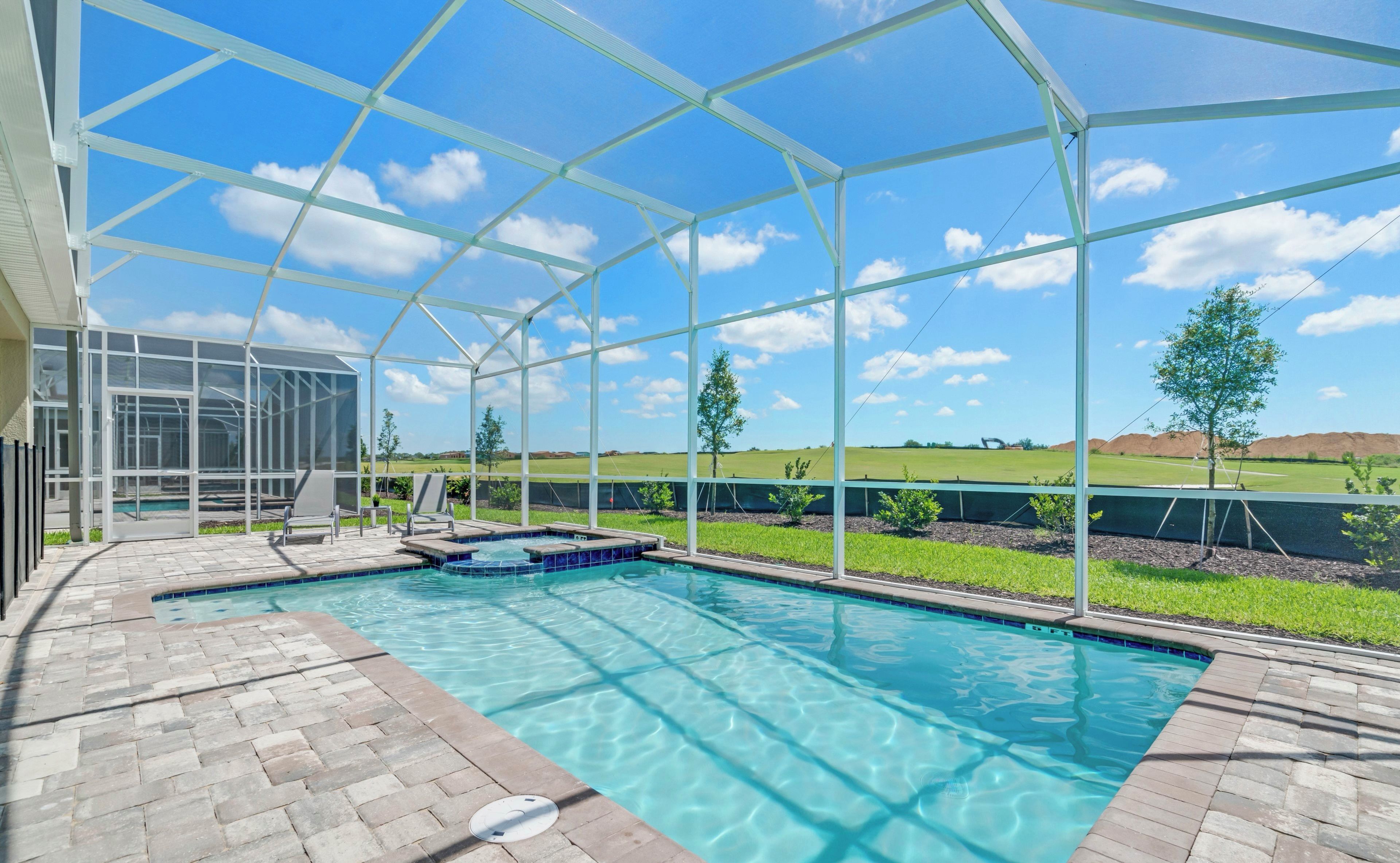 A swimming pool with a glass enclosure, surrounded by a brick patio, and a view of a green landscape.