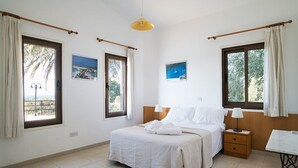Quarto com cama, mesa de cabeceira, mesa e duas janelas com cortinas.