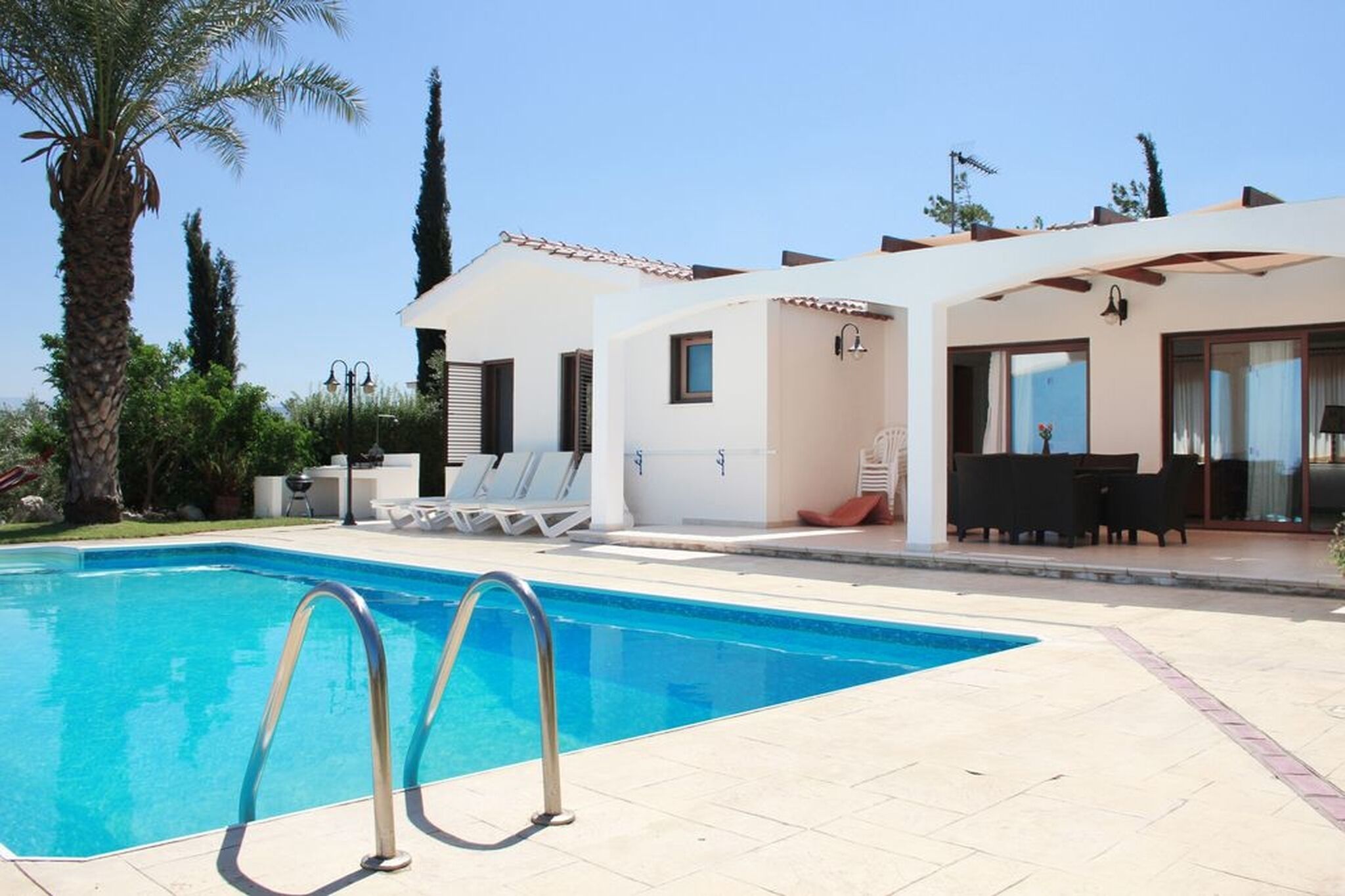 Une piscine avec des chaises longues et un espace patio aménagé avec du mobilier d’extérieur.