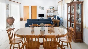 Uma sala de estar com sofá azul, mesa de jantar de madeira e cadeiras, televisão e um armário com portas de vidro.