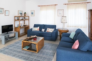 A living room with a blue sofa, a coffee table, a TV, and a bookshelf.