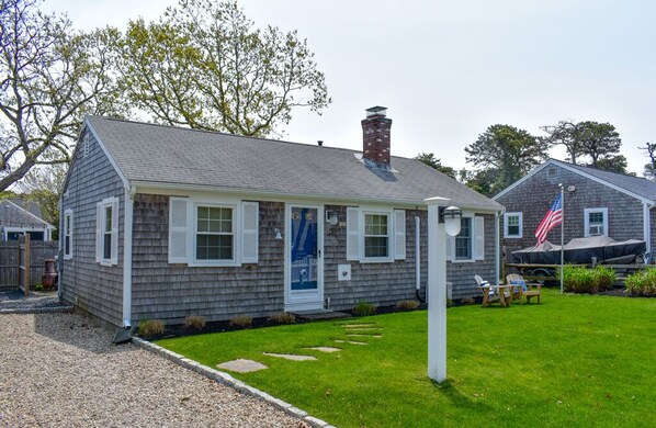 A two-story house with a front porch, a chimney, and a small front yard with a lawn and stepping stones.