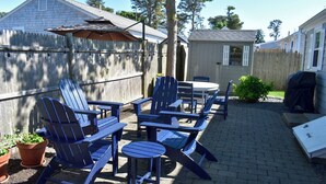 Une terrasse à l’arrière de la maison, avec des fauteuils Adirondack, une table et un barbecue.
