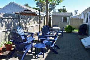 A backyard patio with Adirondack chairs, a table, and a barbecue grill.