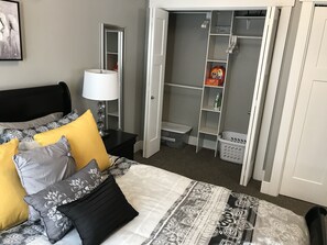 A bedroom with a bed, a nightstand, a lamp, a wardrobe, and a laundry basket.