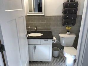 A bathroom with a white sink, a toilet, a trash can, and a towel rack with towels.