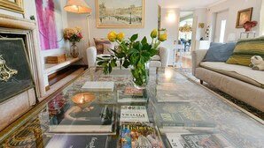 A living room with a glass coffee table displaying magazines, a vase with flowers, and a painting on the wall. - Elegant villa with a park, large private pool, outdoor games, and fitness facilities (verona)