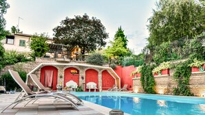 A pool area with lounge chairs, a tiled deck, and a stone wall with greenery. - Elegant villa with a park, large private pool, outdoor games, and fitness facilities (verona)