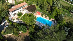 An aerial view of a property with a swimming pool, surrounded by lush greenery and a large house with a tiled roof. - Elegant villa with a park, large private pool, outdoor games, and fitness facilities (verona)