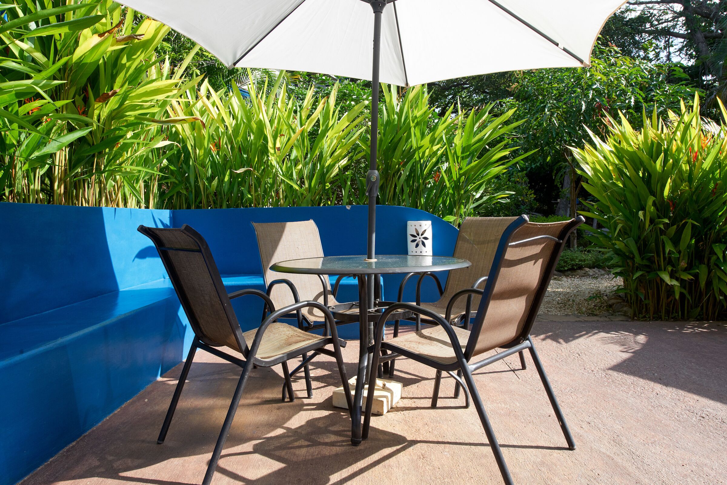 A patio area with a round table and four chairs, a white umbrella, and a blue wall.