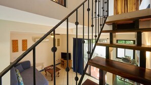 Un escalier avec des marches en bois et des balustrades noires, menant à un espace situé au deuxième étage, comprenant un canapé, une petite table et un téléviseur.