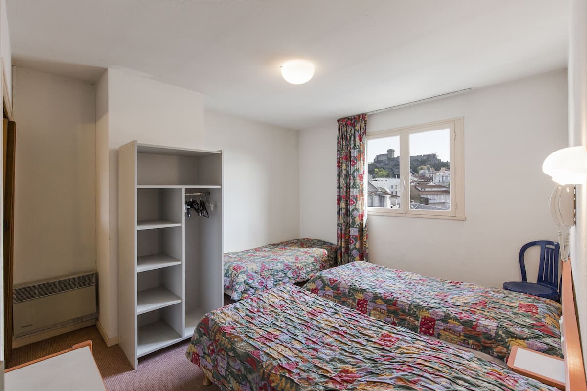 A bedroom with two beds, a wardrobe, and a window with a city view.