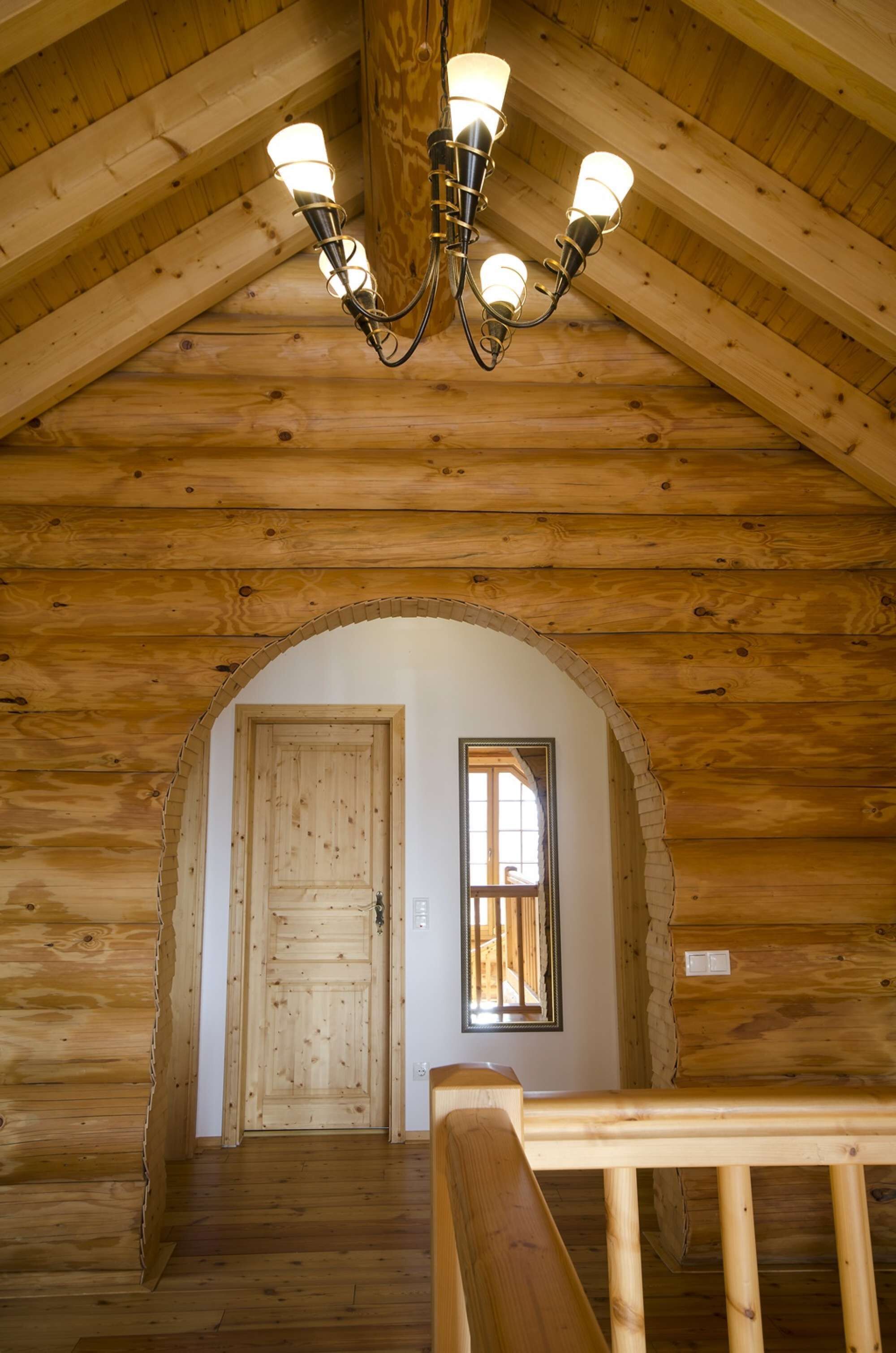 Un intérieur en bois avec un escalier menant à une porte, une fenêtre et un lustre.