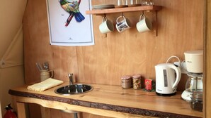 A compact kitchenette with a wooden countertop, a sink, a kettle, a coffee maker, and a shelf with cups and jars. - Tui's Nest Glamping (Villentrois-Faverolles-en-Berry)