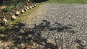 A gravel parking area with a sign indicating a parking area, surrounded by grass and trees. - Tui's Nest Glamping (Villentrois-Faverolles-en-Berry)