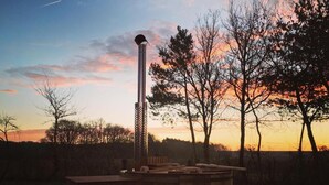 A sauna with a wooden structure and a chimney, surrounded by trees and a sunset sky. - Tui's Nest Glamping (Villentrois-Faverolles-en-Berry)