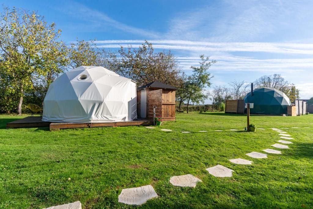 A white geodesic dome tent set on a grassy lawn with a wooden structure nearby.