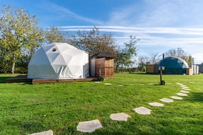 A white geodesic dome tent set on a grassy lawn with a wooden structure nearby. - Tui's Nest Glamping (Villentrois-Faverolles-en-Berry)