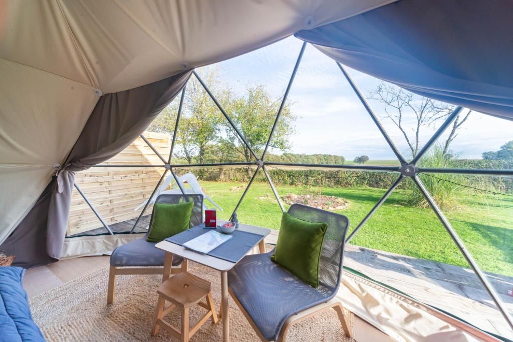 A tent with a table and chairs, a view of a grassy field, and a clear sky.