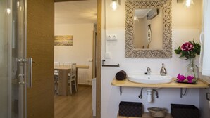 Un baño con tocador de madera, espejo con marco decorativo, lavamanos y un jarrón con flores.